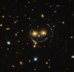 Smile! Die „Gesichtszüge“ dieses Galaxienclusters in einem Hubble-Foto sind verzerrte Bilder dahinter liegender Galaxien.